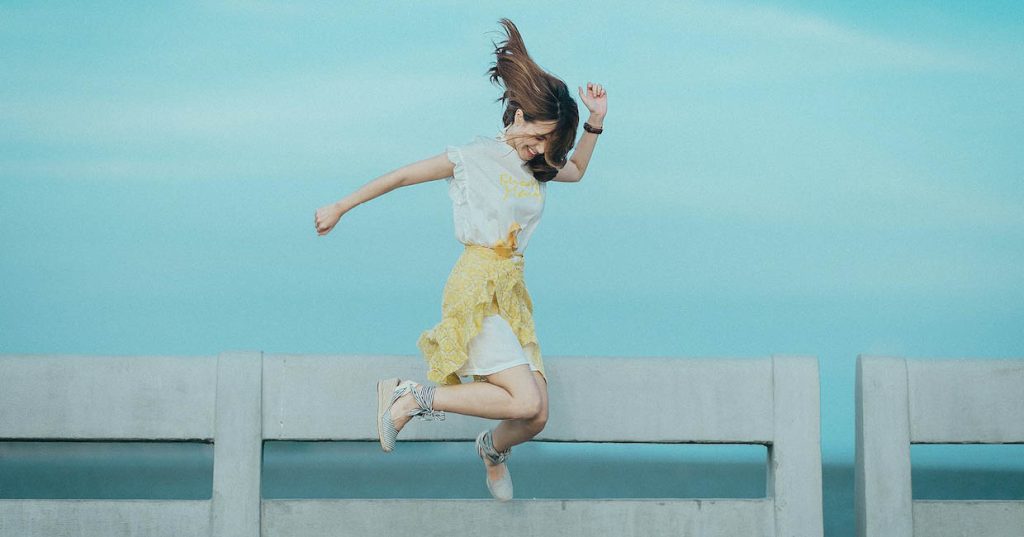 Girl jumping with a fence and water behind her.