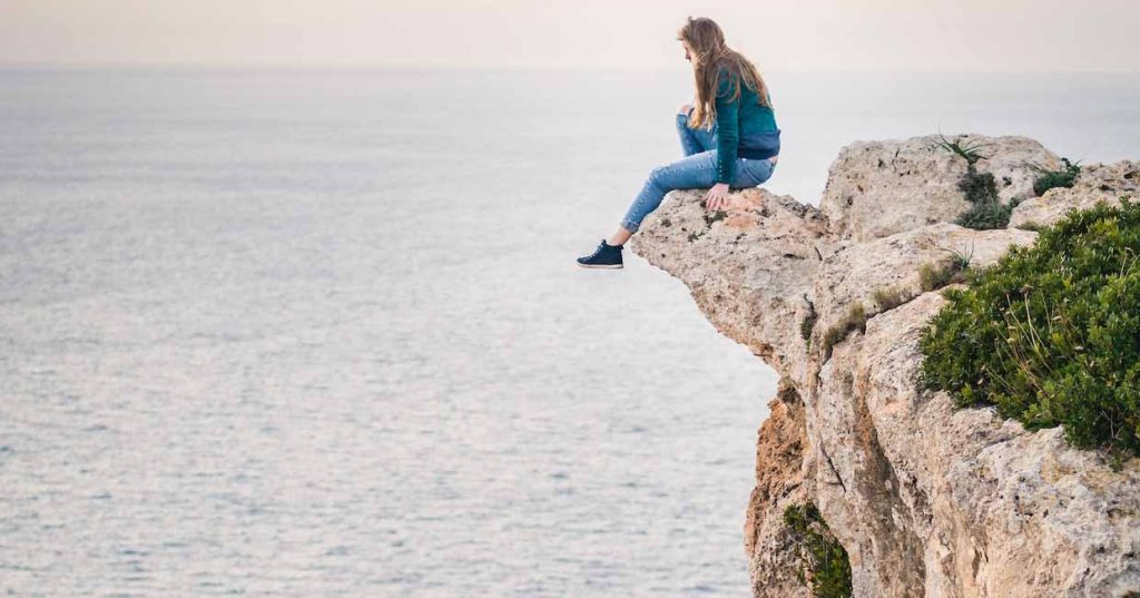 person sitting on cliffside overlooking water
